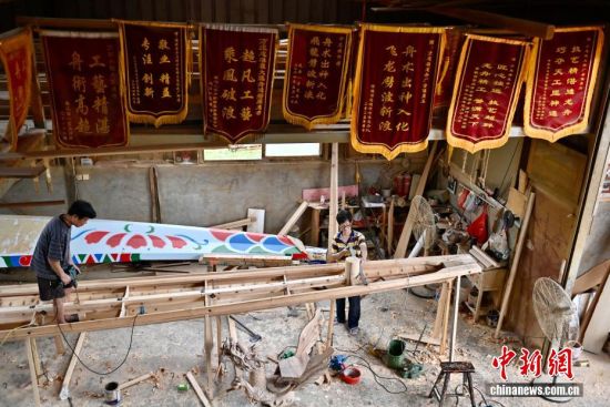图为6月8日,在方庄村“龙舟世家”方忠雄龙舟厂内,匠人正在做龙舟,上面挂满了顾客送来的锦旗。中新社记者 王东明 摄 图为6月8日,在方庄村“龙舟世家”方忠雄龙舟厂内,匠人正在做龙舟,上面挂满了顾客送来的锦旗。中新社记者 王东明 摄